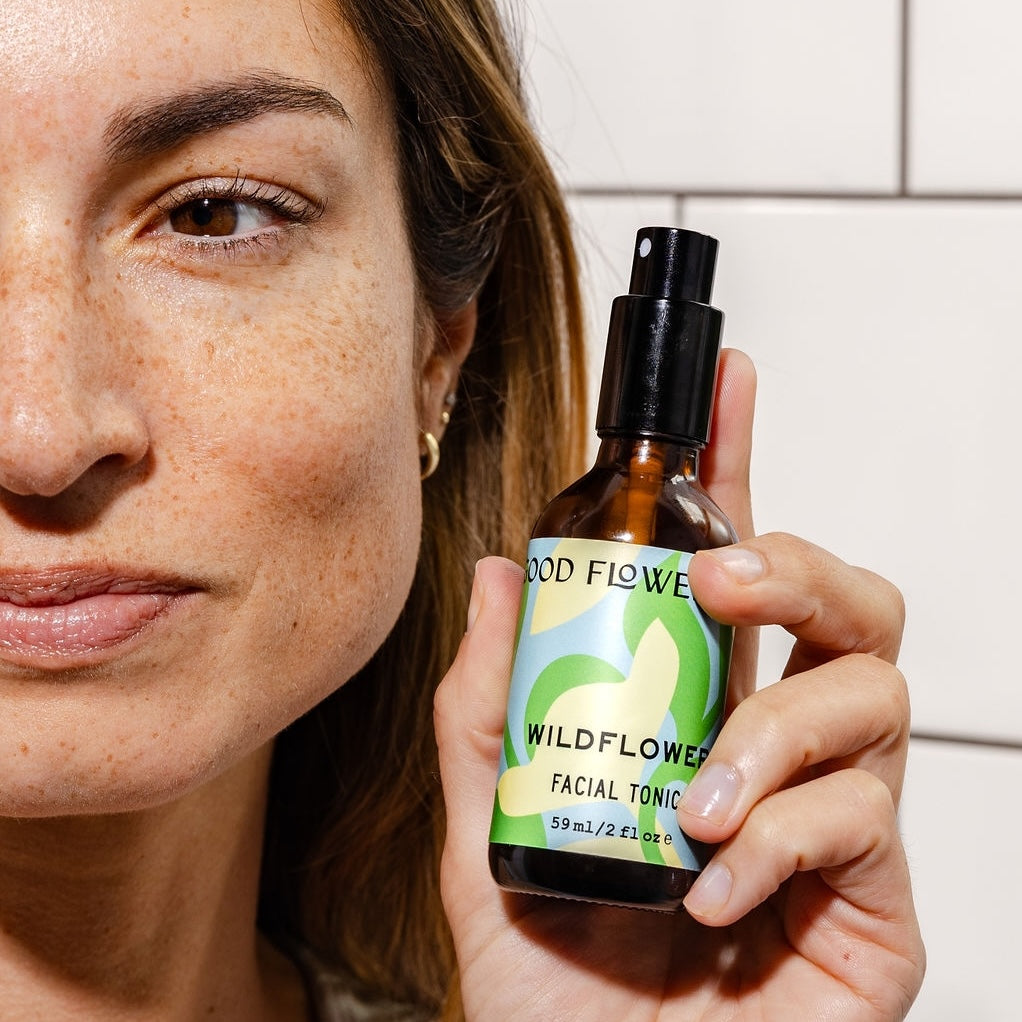 Person holding a bottle of 'Wildflower' facial tonic with a neutral background