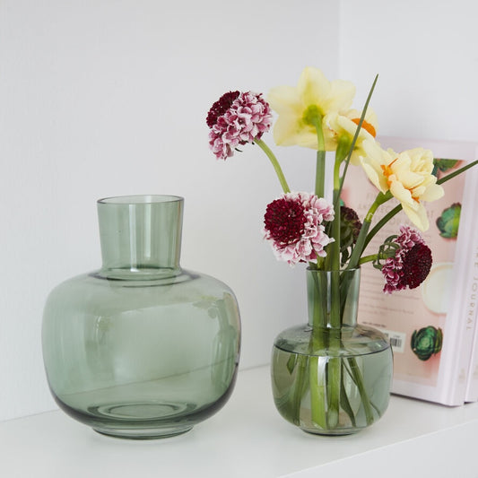 Green vase with flowers on a white surface