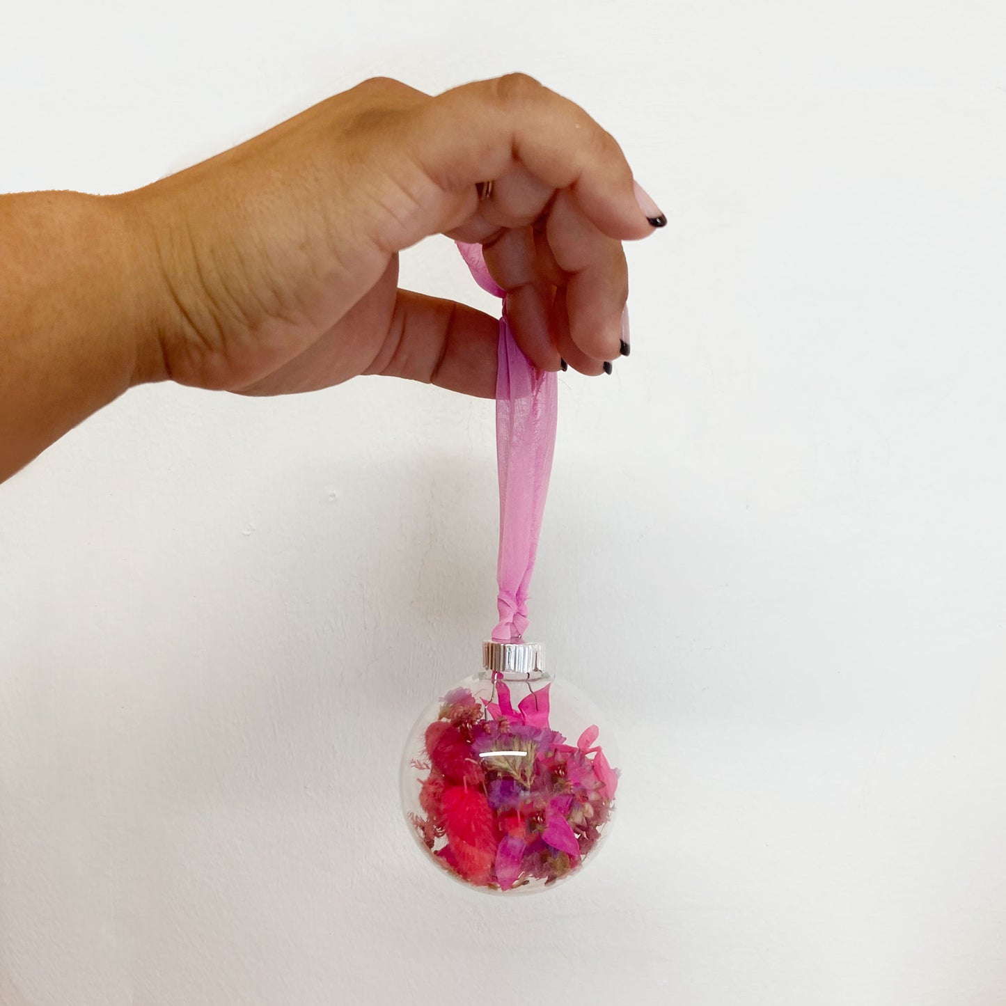 Hand holding a decorative ornament with pink ribbon against a white background