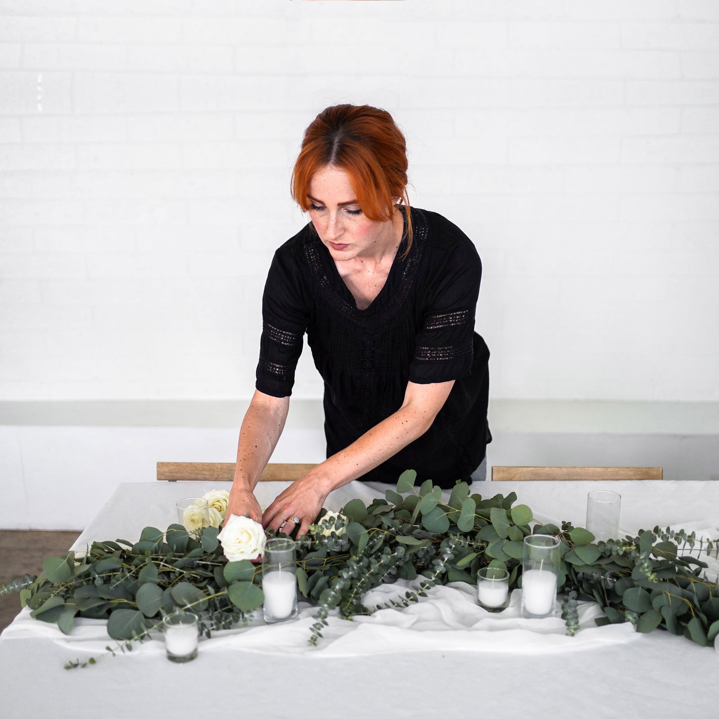 Florist adjusts Eucalyptus Garland with white roses with votive candles