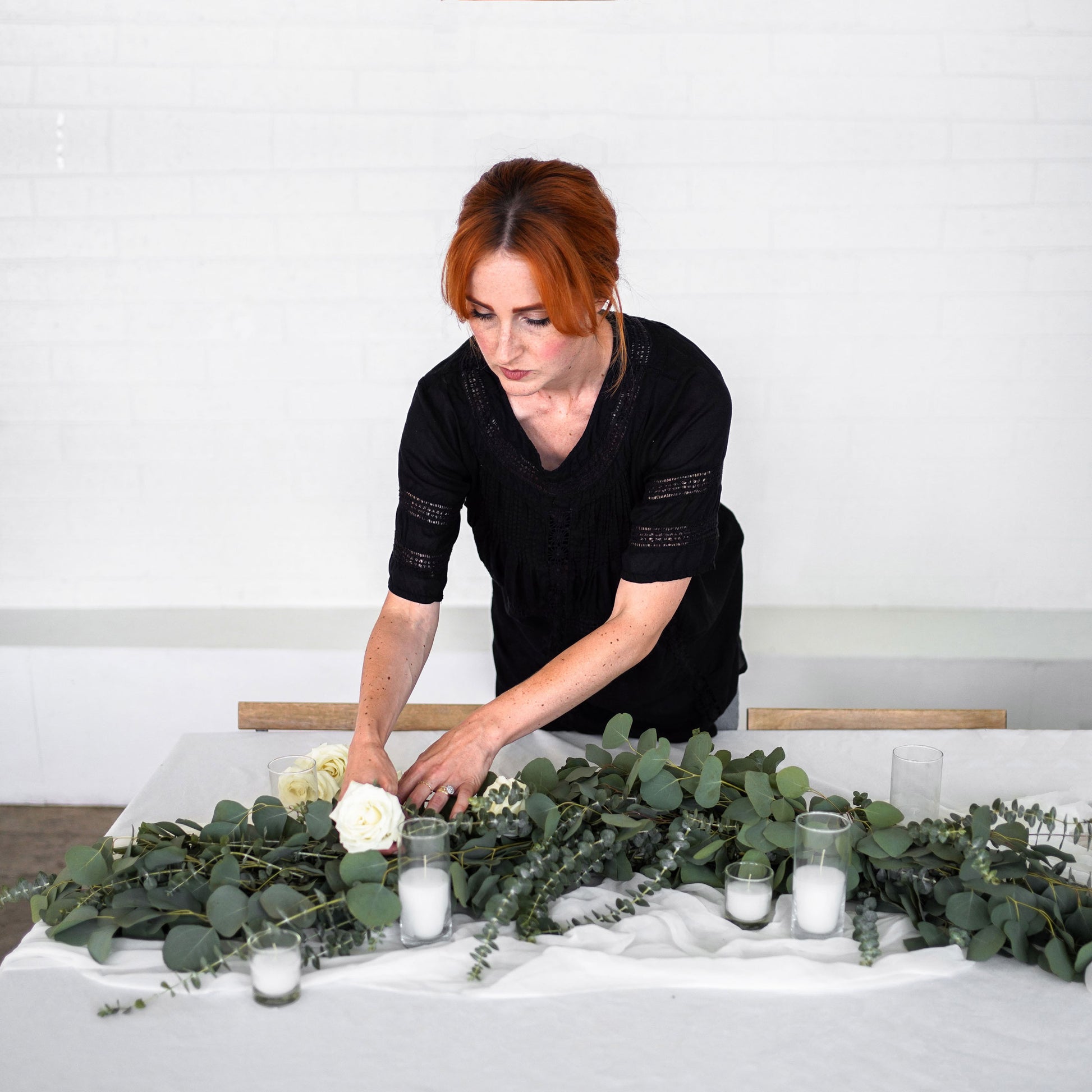Florist adjusts Eucalyptus Garland with white roses with votive candles