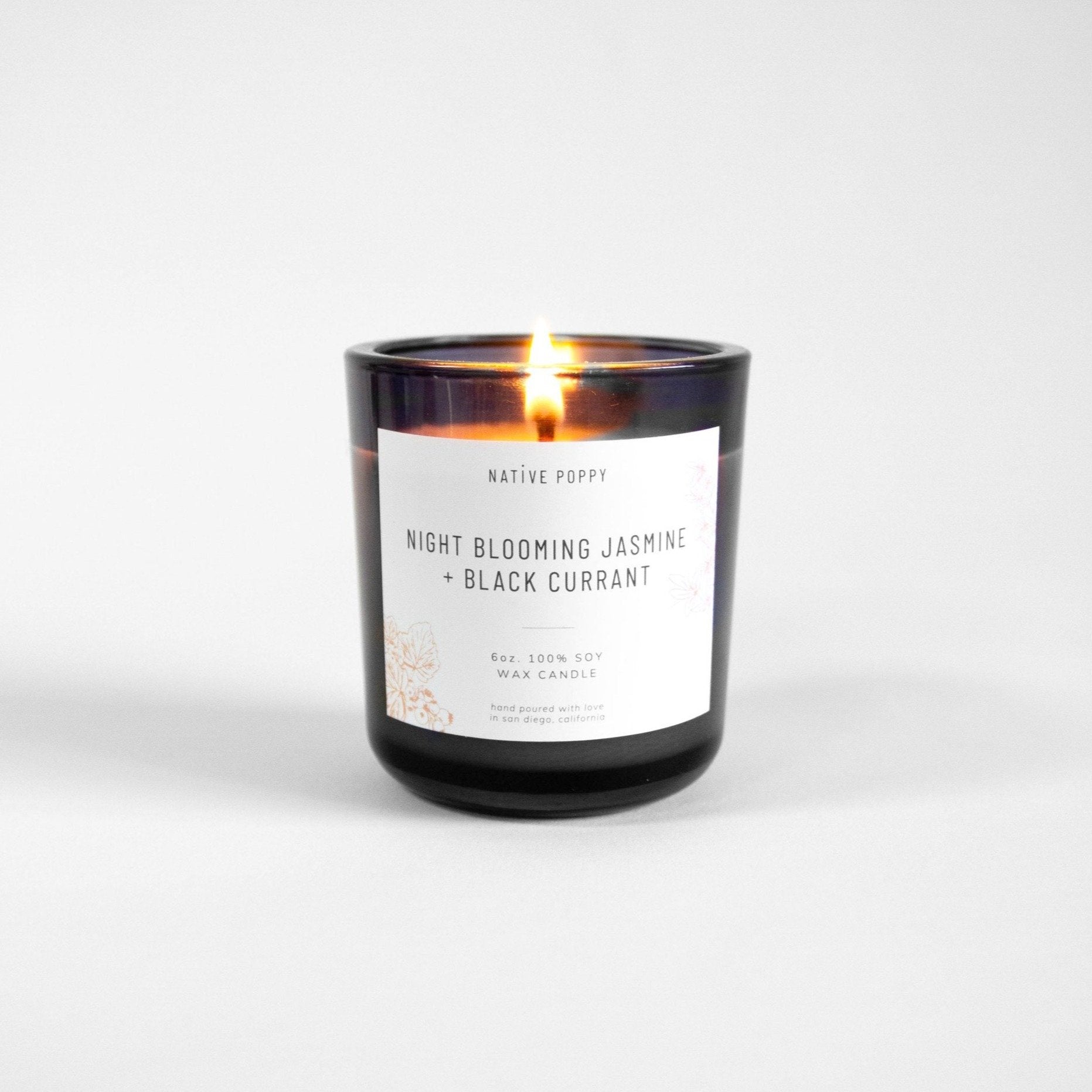 Night Blooming Jasmine + Black Currant Candle lit with glowing flame in grey glass jar