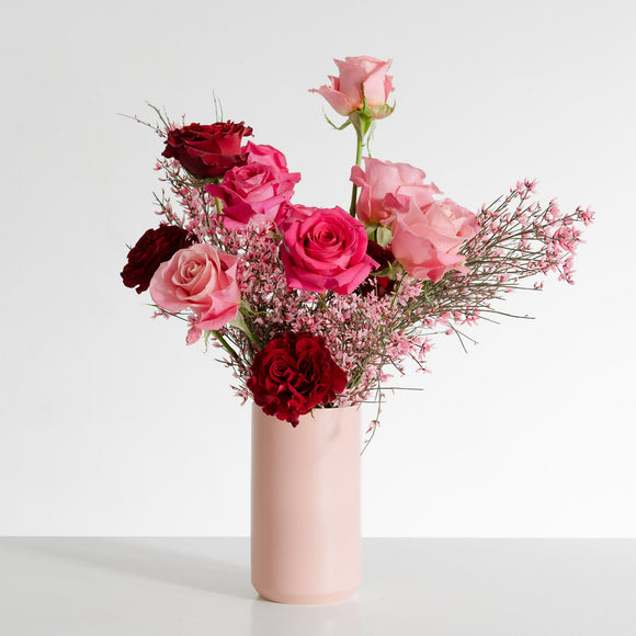 Red and pink roses in a blush pink vase