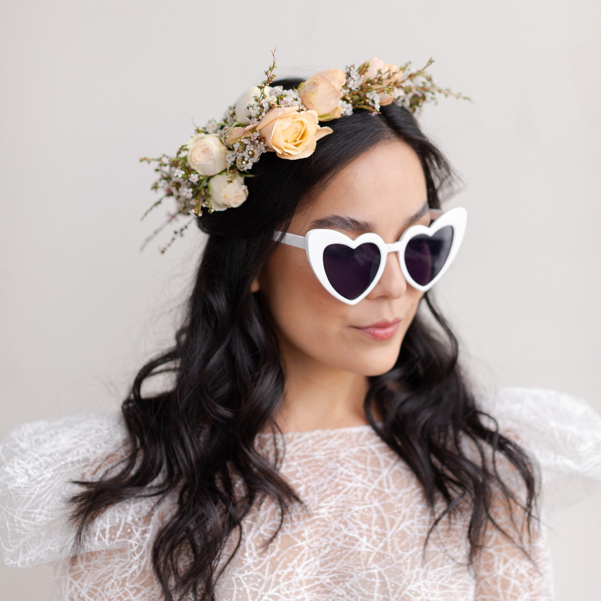 Woman with dark hair wearing Grace flower crown and heart sunglasses